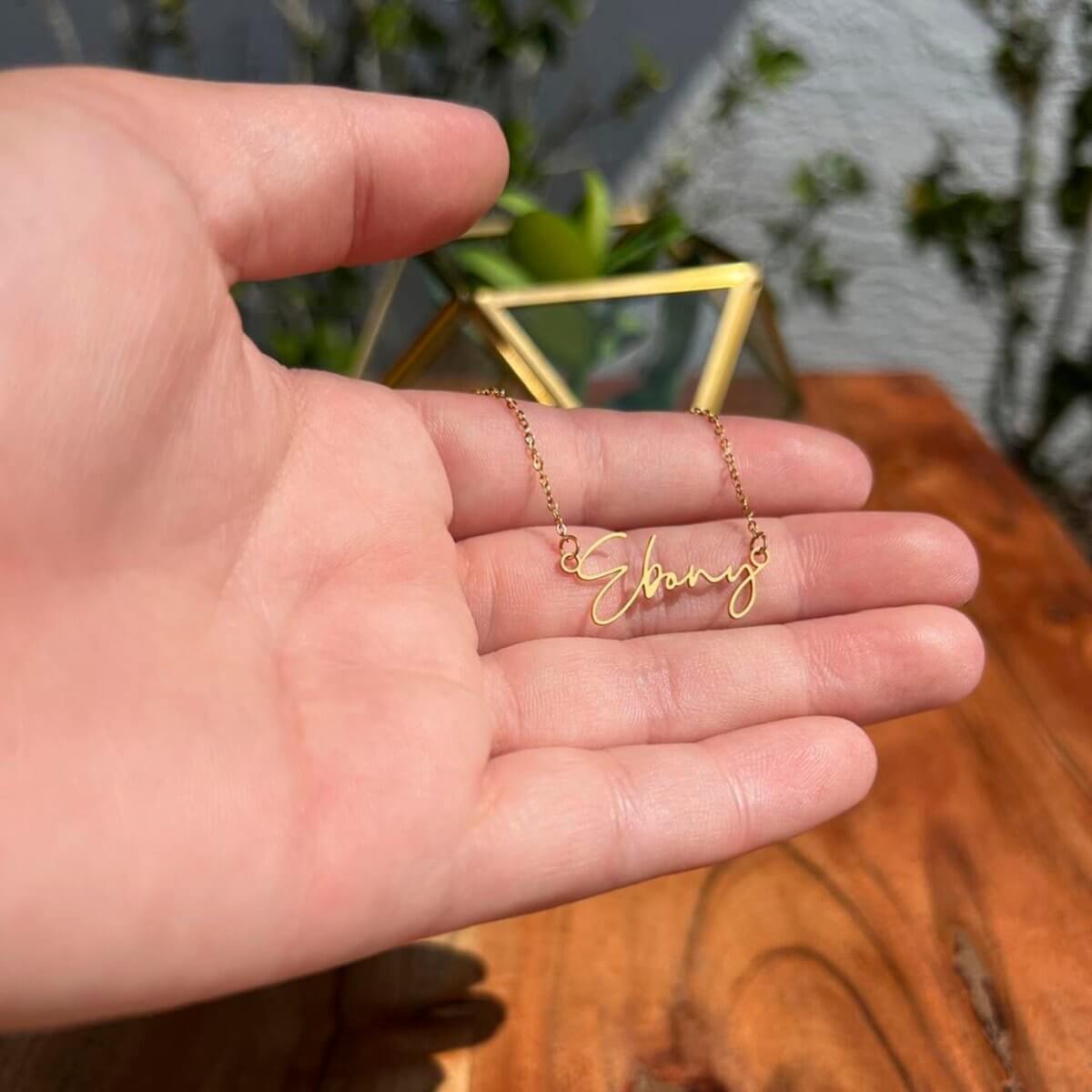 TrueScript Signature Necklace held in hand, featuring personalized name 'Ebang,' crafted in polished gold finish.