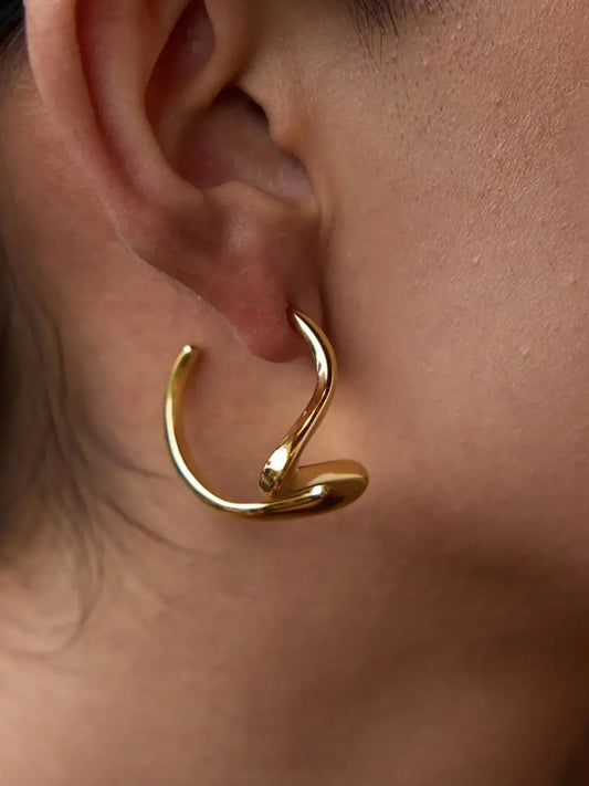 Close-up of a woman's ear showcasing elegant Golden Coil Studs in 18K gold, curved design highlighting its unique style.